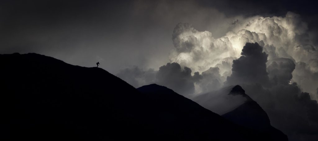 Vers d'autres Éternités Photographie d’Alexandre Deschaumes – Col d’Anterne, massif du Haut-Giffre : silhouette d’un coureur sur la crête devant un cumulonimbus orageux, ambiance mystique et dramatique