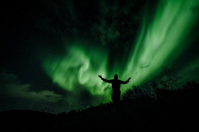 Silhouette sous les aurores boréales – Norvège Silhouette humaine se détachant sous des aurores boréales dans le ciel nocturne de Norvège